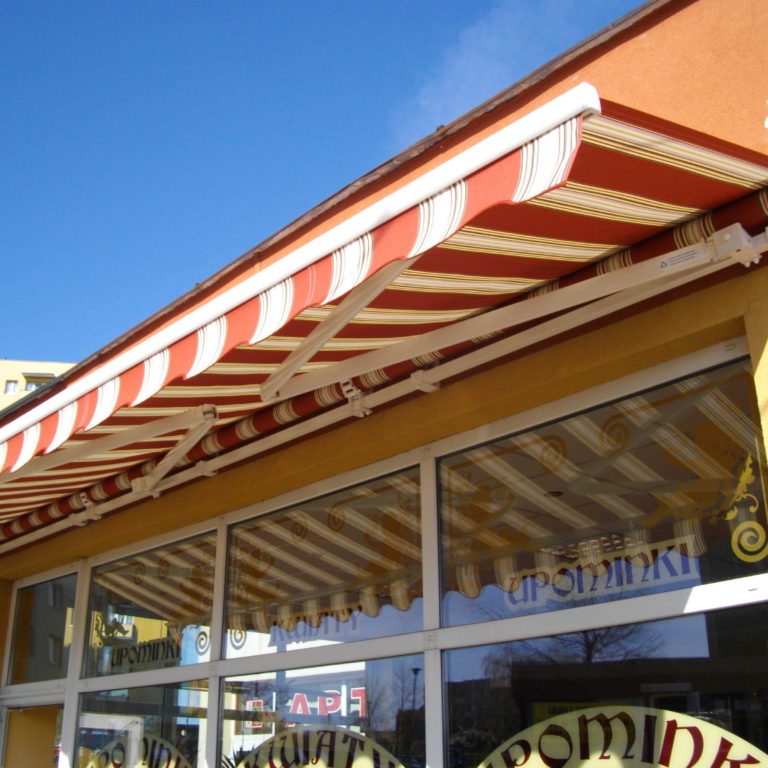 Markiza tarasowa w biało-pomarańczowy wzór, zamontowana nad witryną sklepową