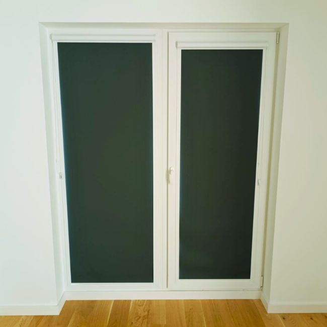 Rolety w kasecie zamontowane na białym oknie w nowoczesnym salonie.