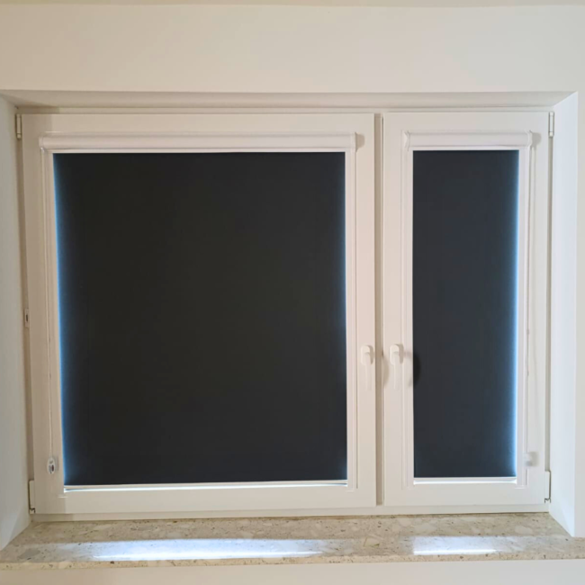 Rolety w kasecie zamontowane na białym oknie w nowoczesnym salonie.