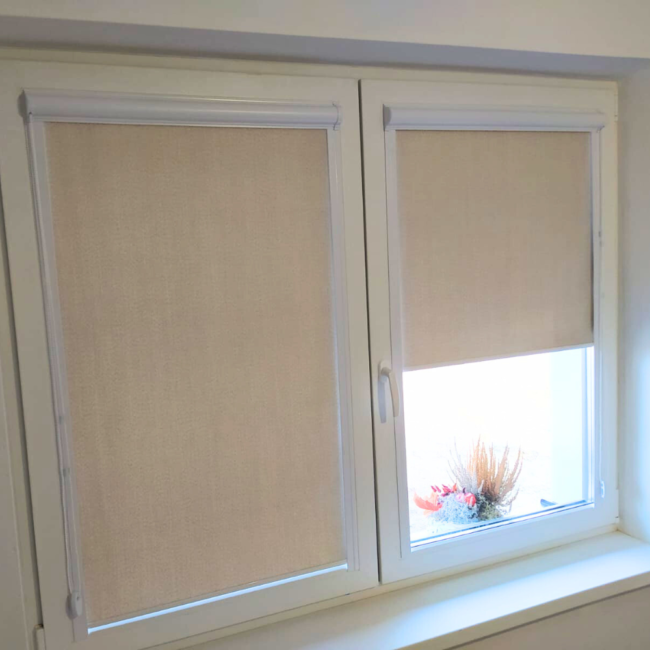 Rolety w kasecie zamontowane na białym oknie w nowoczesnym salonie.