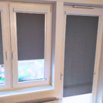 Rolety w kasecie zamontowane na białym oknie w nowoczesnym salonie.