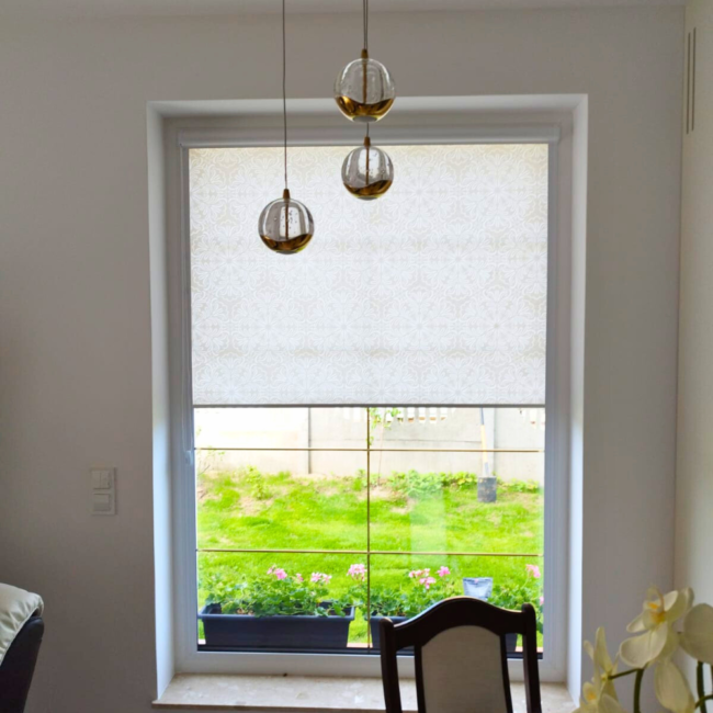 Rolety w kasecie zamontowane na białym oknie w nowoczesnym salonie.