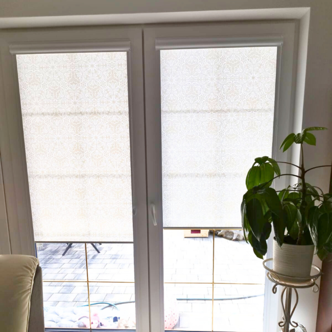 Rolety w kasecie zamontowane na białym oknie w nowoczesnym salonie.