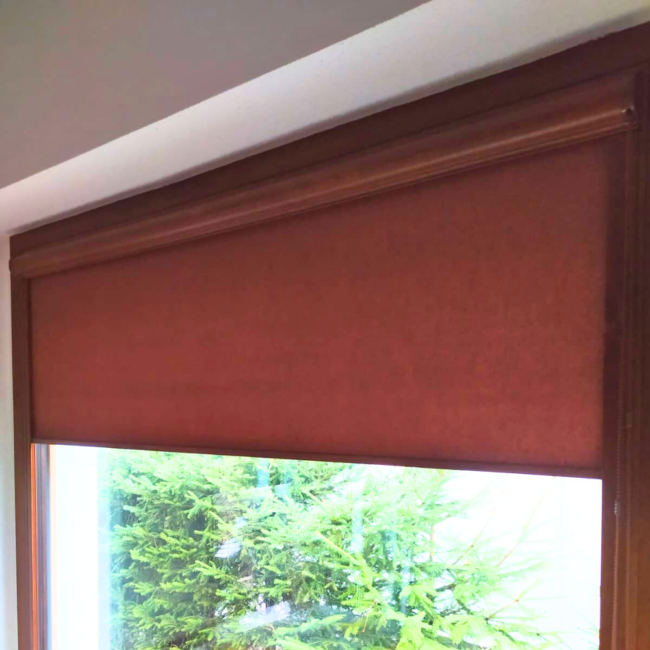 Rolety w kasecie zamontowane na białym oknie w nowoczesnym salonie.