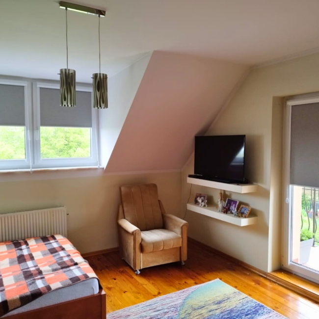 Rolety w kasecie zamontowane na białym oknie w nowoczesnym salonie.