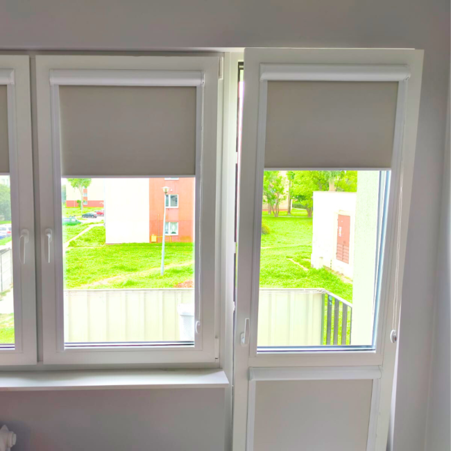 Rolety w kasecie zamontowane na białym oknie w nowoczesnym salonie.