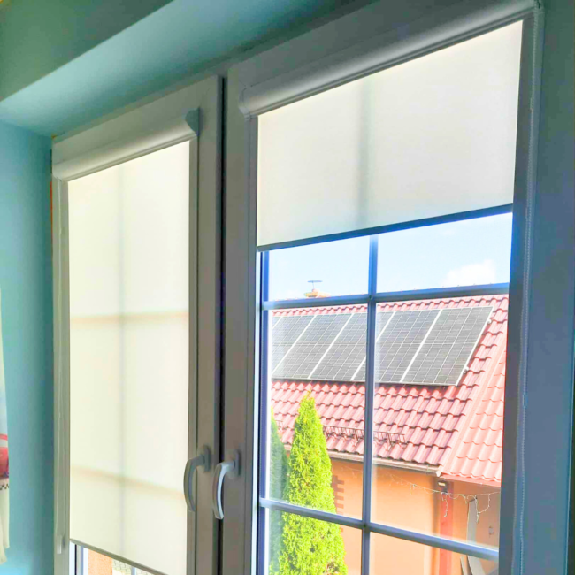 Rolety w kasecie zamontowane na białym oknie w nowoczesnym salonie.