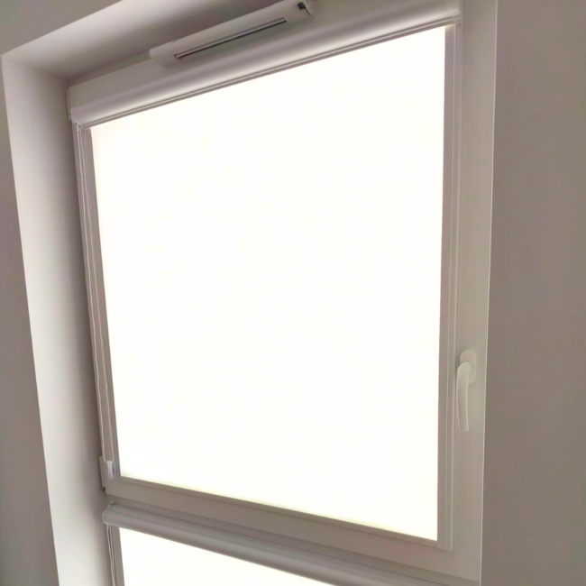 Rolety w kasecie zamontowane na białym oknie w nowoczesnym salonie.