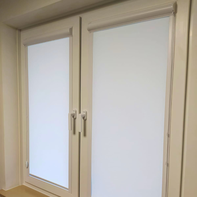 Rolety w kasecie zamontowane na białym oknie w nowoczesnym salonie.