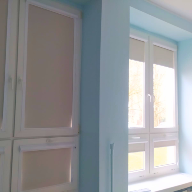 Rolety w kasecie zamontowane na białym oknie w nowoczesnym salonie.