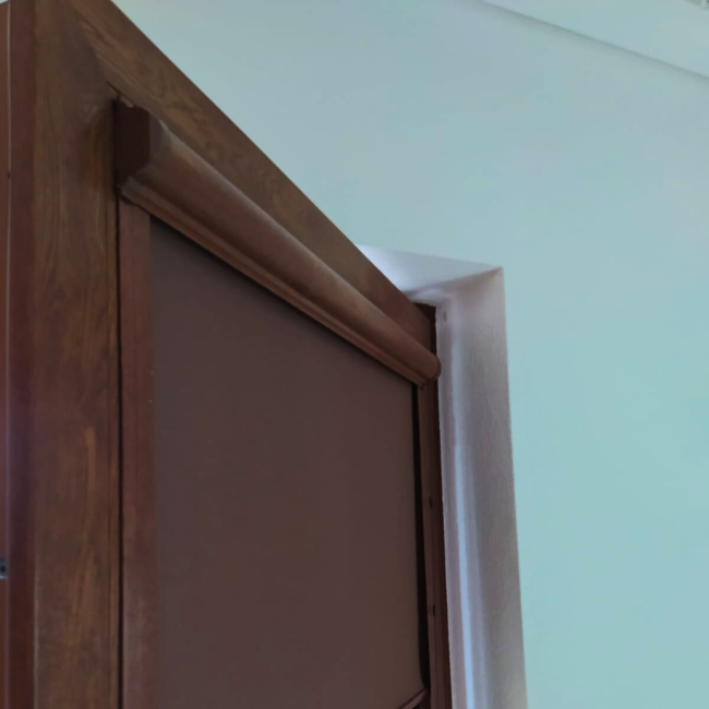 Rolety w kasecie zamontowane na białym oknie w nowoczesnym salonie.