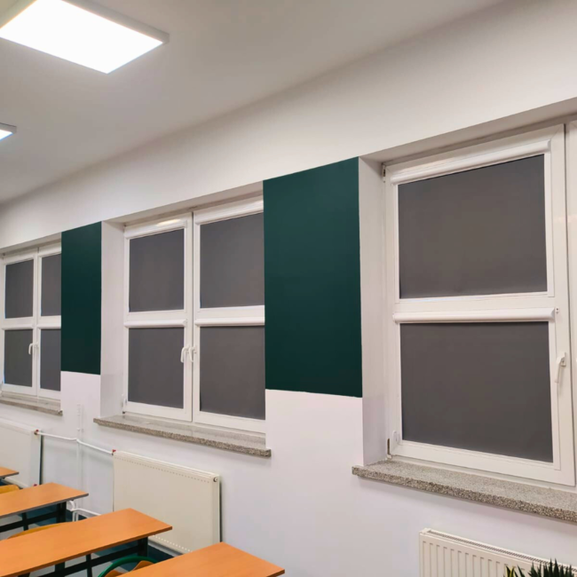 Rolety w kasecie zamontowane na białym oknie w sali lekcyjnej