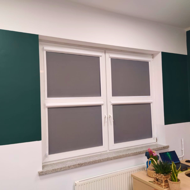 Rolety w kasecie zamontowane na białym oknie w sali lekcyjnej