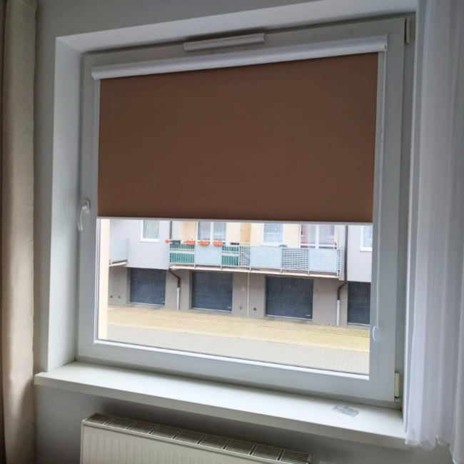 Rolety w kasecie zamontowane na białym oknie w nowoczesnym salonie